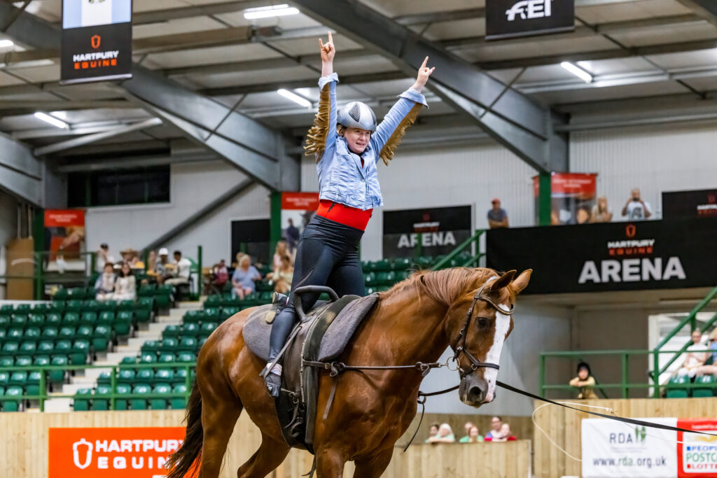 Lizzie on a horse standing up in the stirrups and reaching up