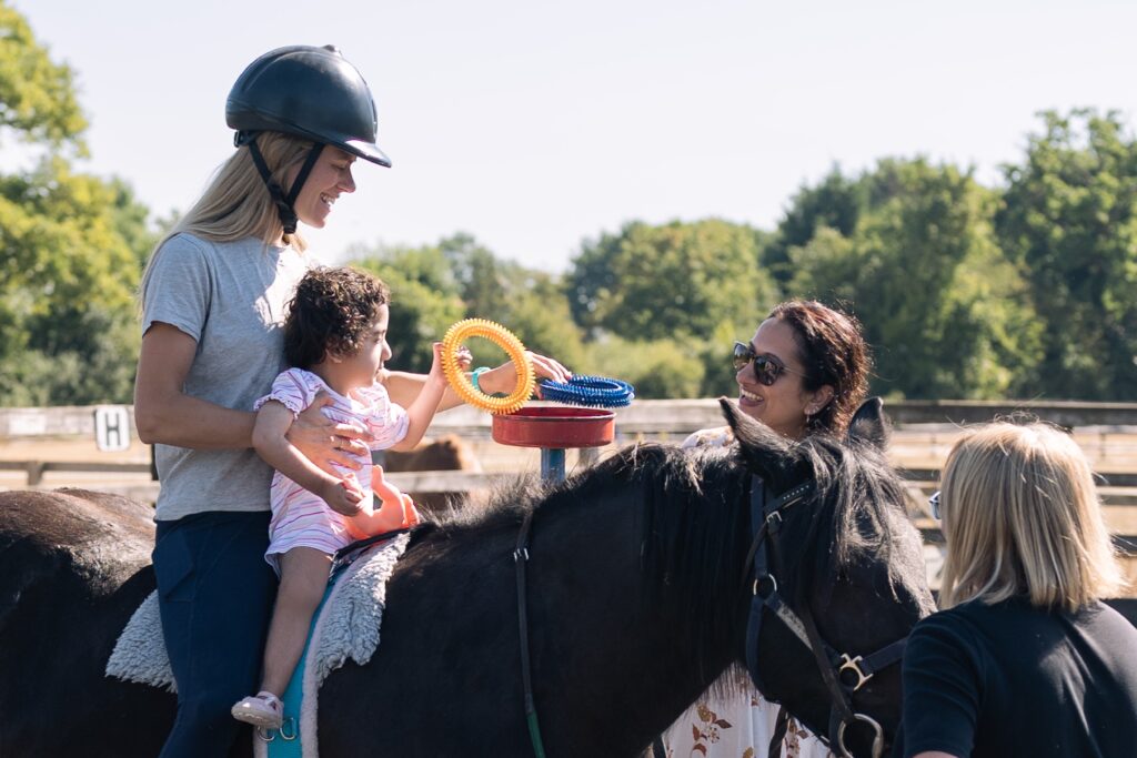 Physio and young client sat on pony supported by volunteer and mother