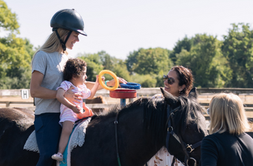 Physio and young client aged 3 sat on pony supported by volunteer and mother