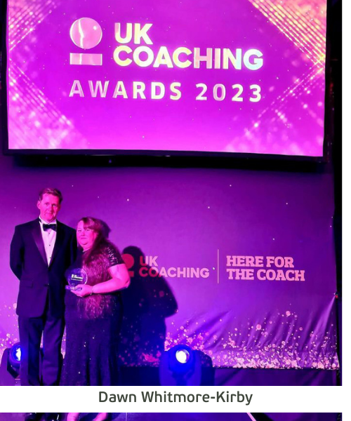 Dawn Whitmore-Kirby receives her award at the UK Coaching Awards Ceremony. She stands with her husband under a large UK Coaching banner.