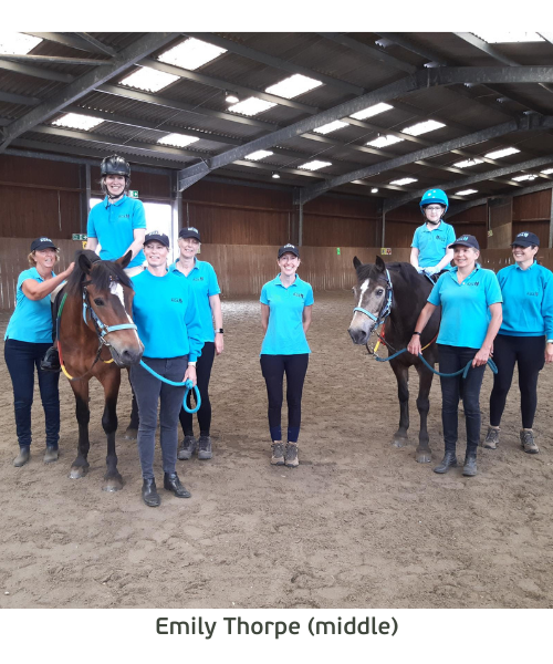 Emily stands proudly at South Downs RDA between two horses and riders and four volunteers.