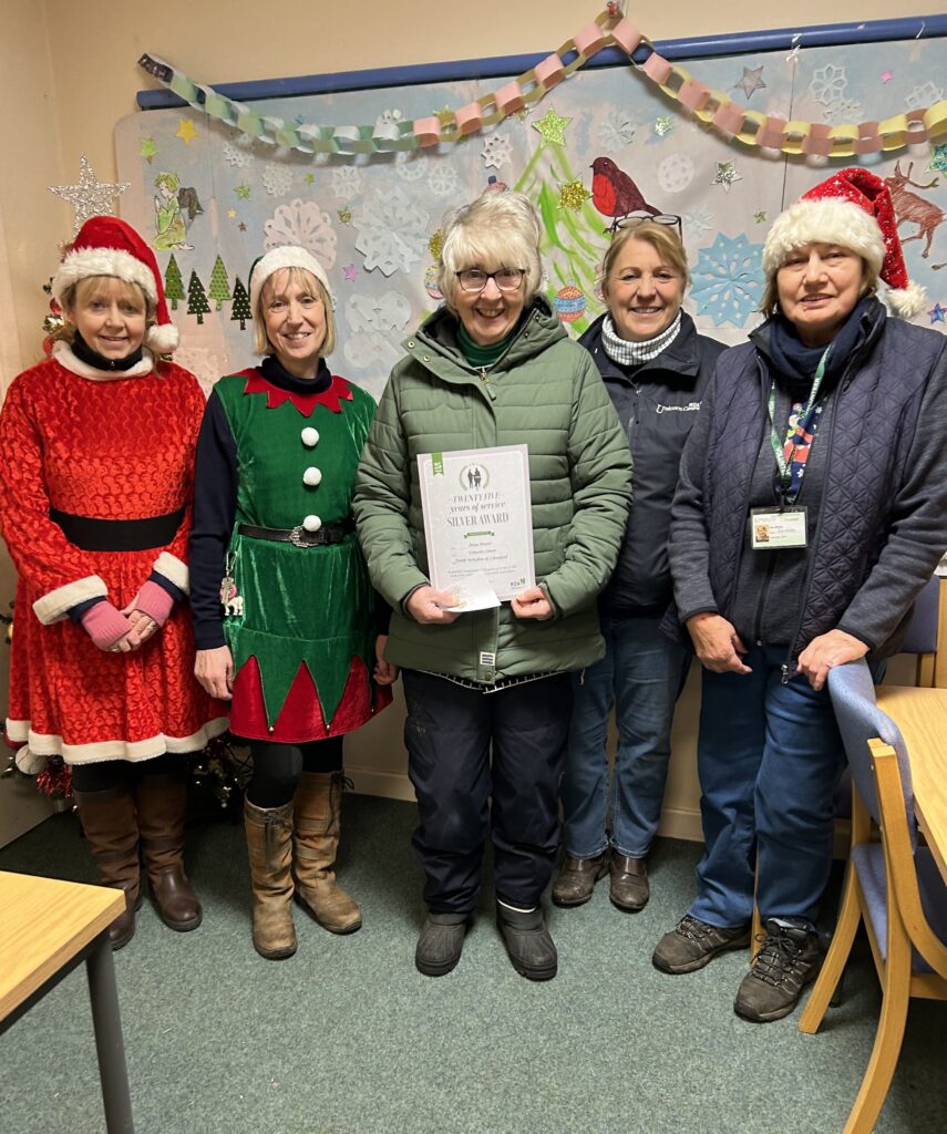 Anna Power receives her long service award. She is in the middle of four other people, who are dressed in Christmas fancy dress.