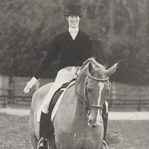 Jane sits on top of a horse, in formal dressage wear.
