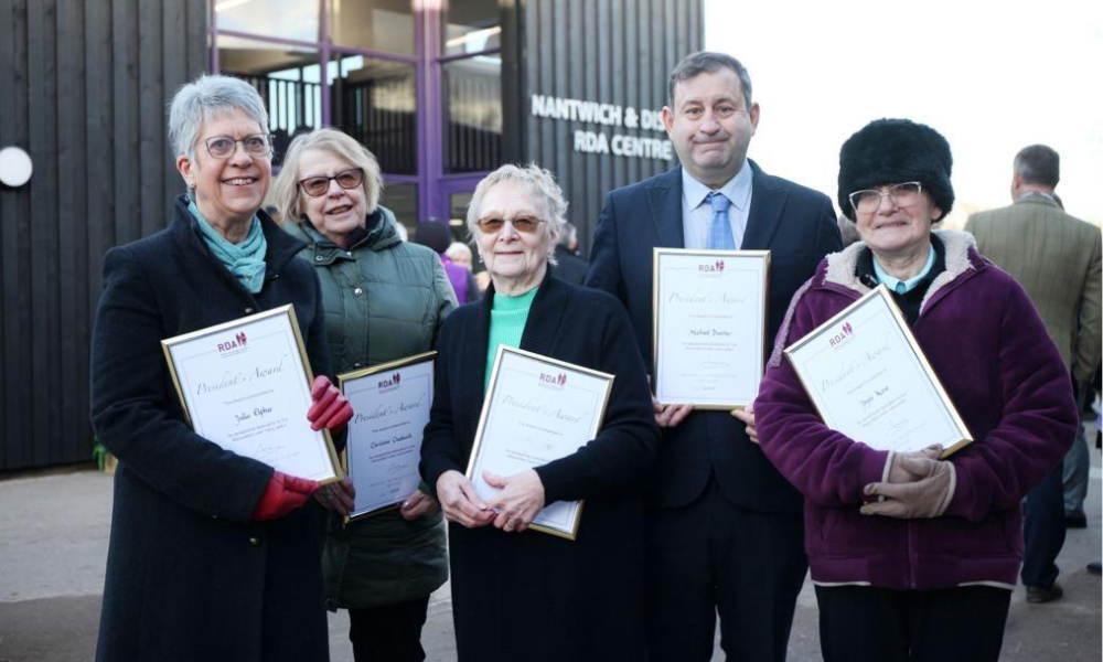 Five award winners holding their certificates presented to them by HRH Princess Anne, they all smile happily, wrapped up in winter coats.