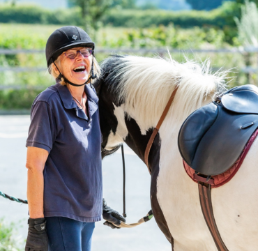 Volunteer laughing next to a piebald pony.