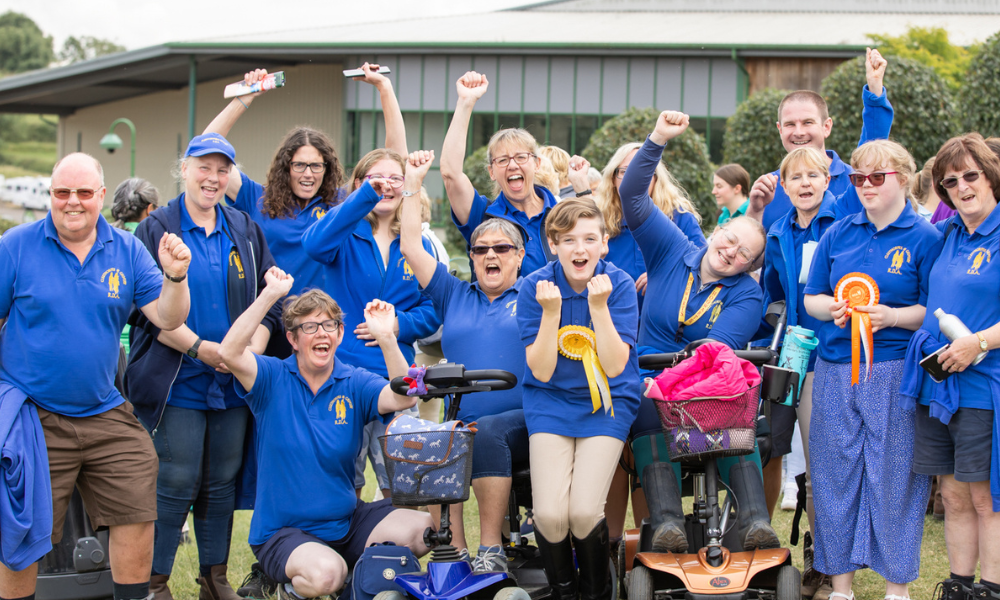 RDA Cleethorpes and Grimsby cheer and celebrate their achievements, competitors at the front hold their rosettes and the volunteers cheer them on. All are wearing matching royal blue polo shirts