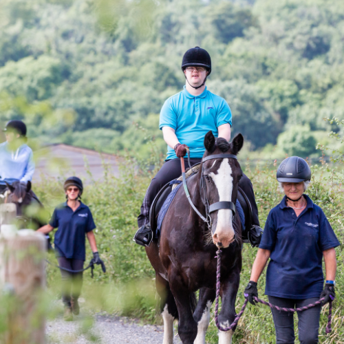 A rider is being led by a volunteer. The rider wears a blue polo.