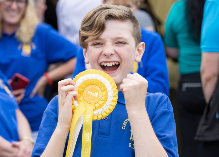 A young RDA participant cheers, with a shiny yellow rosette in his hand. He is wearing a blue polo shirt.