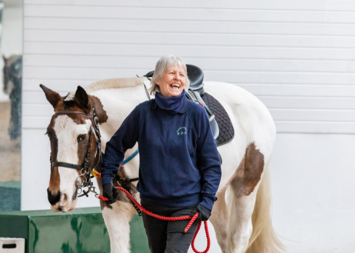 A woman leads a skewbald pony. She wears a blue raincoat.