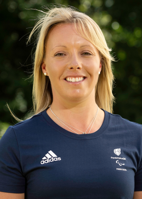 Sophie smiles, she has long blond hair. She wears a navy blue official paralympics team shirt.