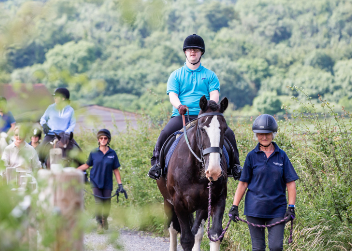 A rider is being led by a volunteer. The rider wears a blue polo.