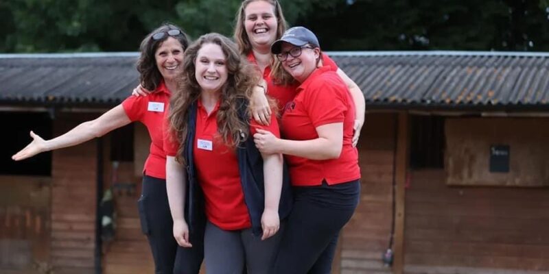 Four ladies wearing red tops huddled together for a group photo and smiling towards the camera