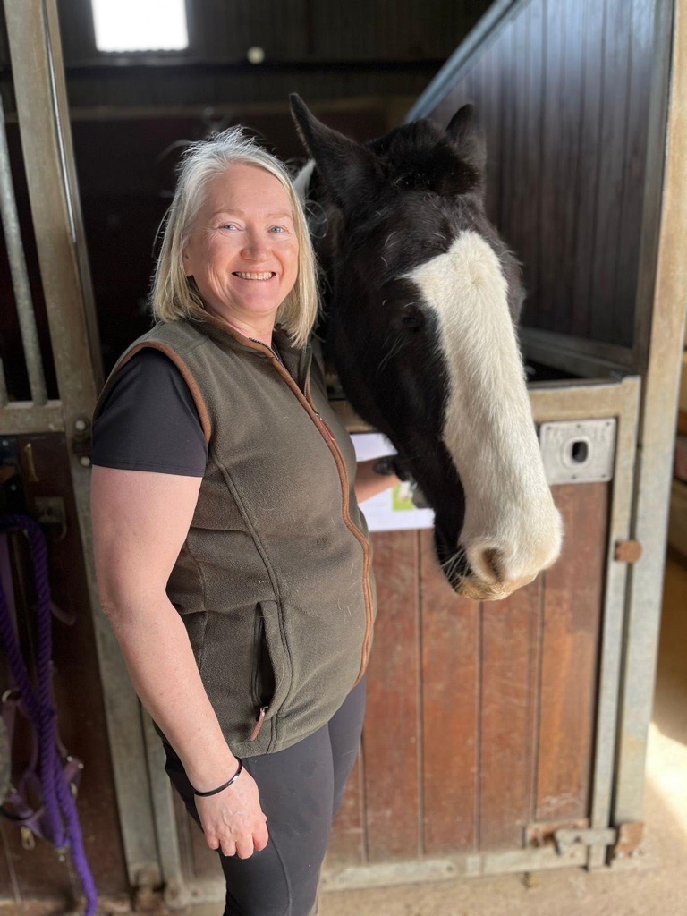 A woman with blonde hair stood next to a horse in a stable.