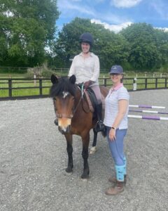 A woman riding a horse and women stood on the ground next to the horse.