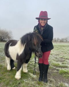 A woman wearing a read hat while stood next to a Shetland pony