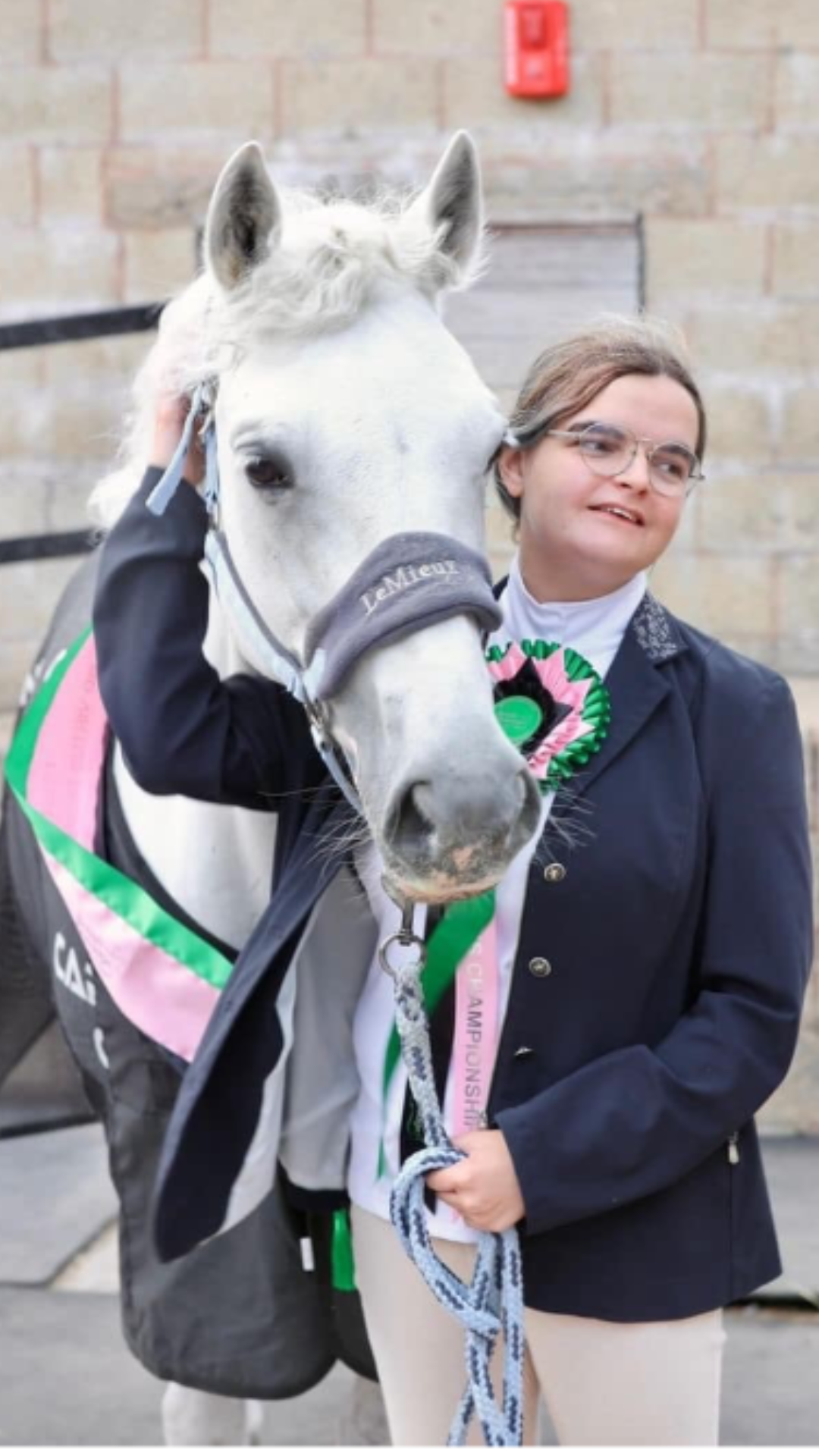 Mia stood next to her grey horse with a rosette